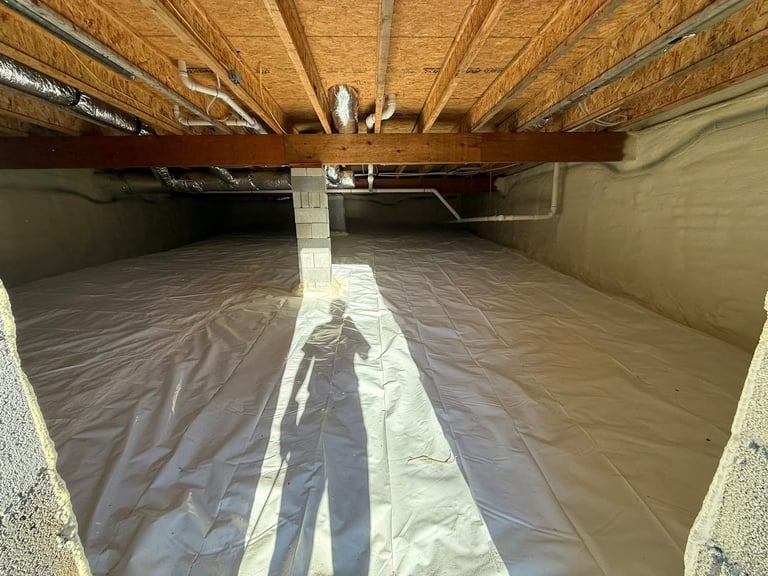 Interior of a crawl space with plastic vapor barrier lining the floor and wooden beam supports above