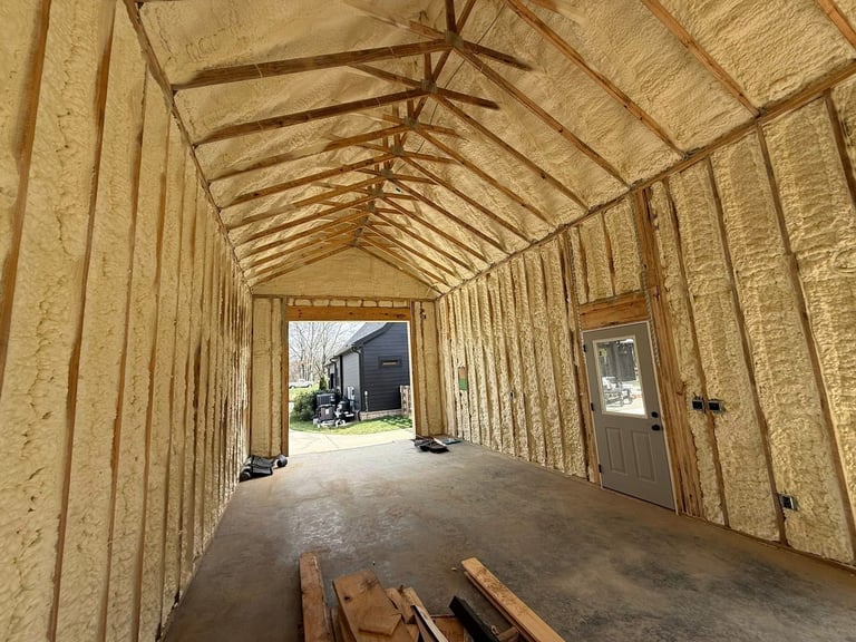 Interior of a wooden barn under construction with exposed framing, concrete floor, and open doorway showing outdoor entrance