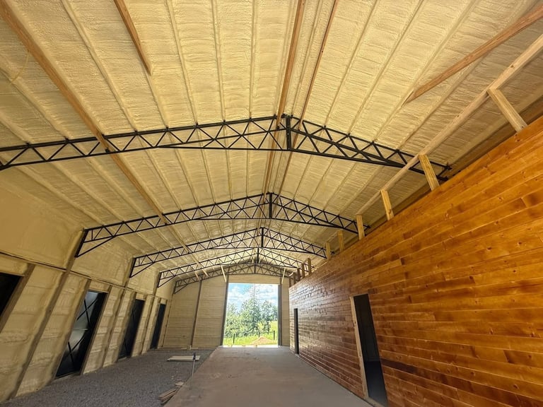 Interior of a covered barn walkway with arched metal framework, cream-colored roof panels, and brick walls on one side