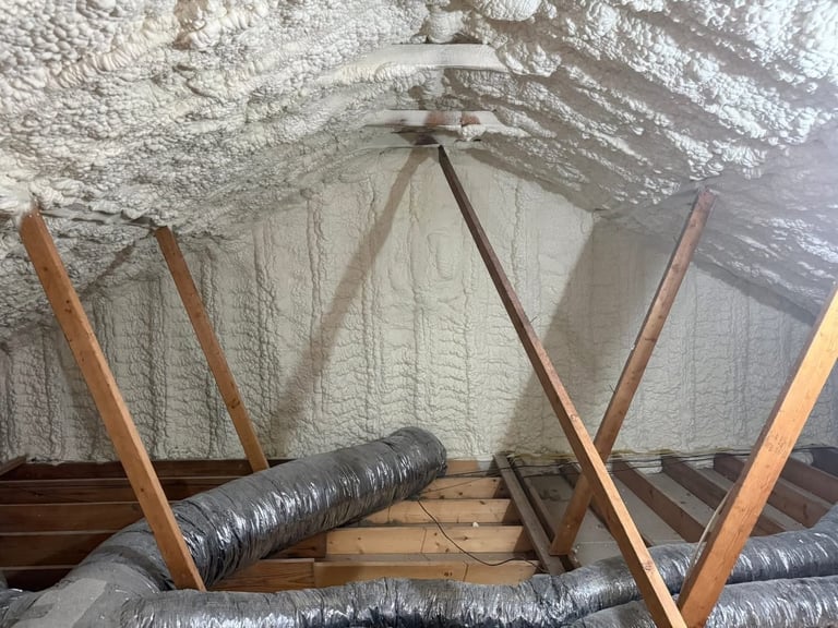 Attic insulation installation with exposed wooden beams, ductwork, and fibrous insulation material beneath white ceiling